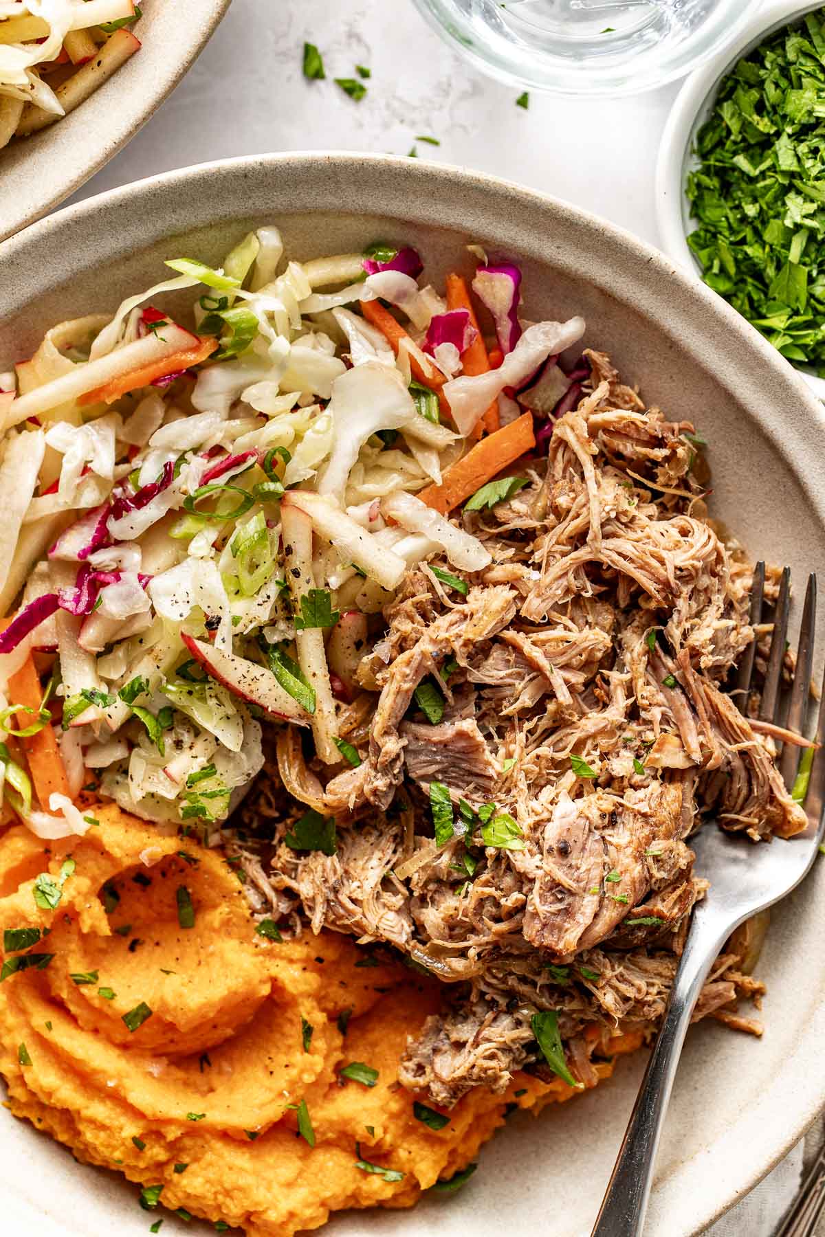 Close up view of a Crockpot Apple Cider Pork Bowl topped with black pepper and fresh herbs. 