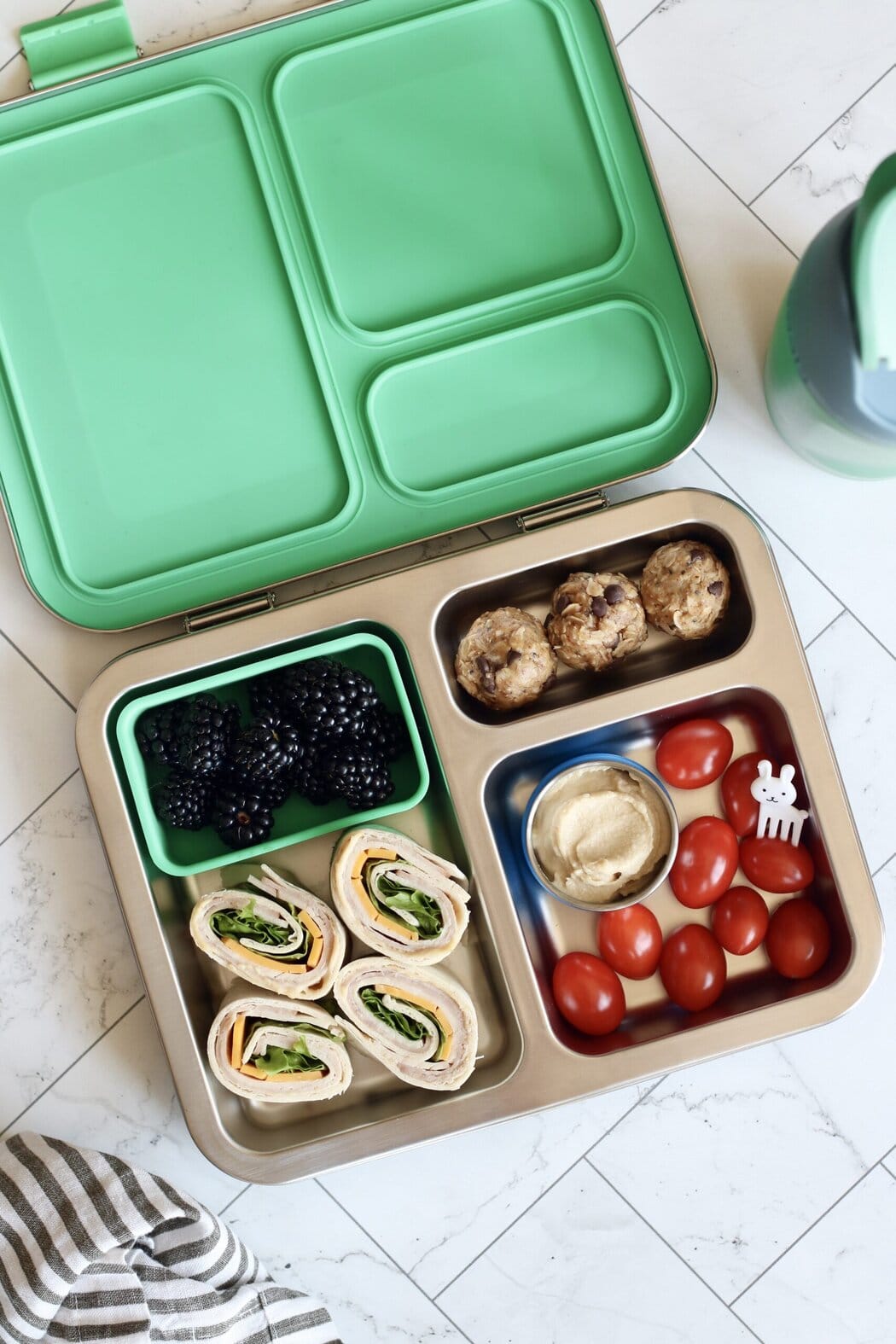 Overhead view of an open lunch box filled with cherry tomatoes, blackberries, energy balls, and tortilla roll ups. 