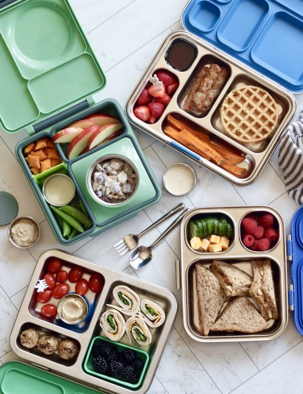 Several kid's lunchboxes open and filled with whole foods.
