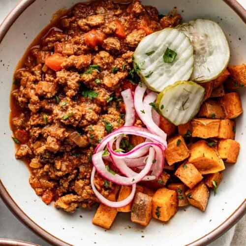 Overhead view of a Sloppy Joe Bowl filled with freshly roasted sweet potatoes, pickled red onions, and crisp pickle chips topped with fresh herbs.