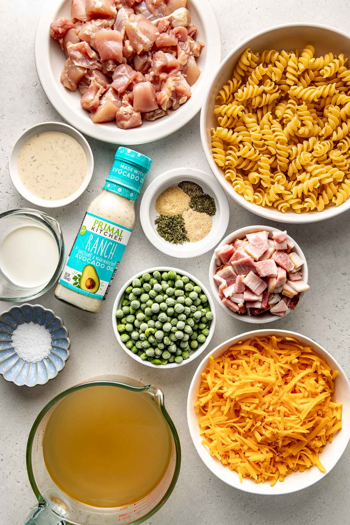 Overhead view of a variety of ingredients for One-Pot Chicken Bacon Ranch Pasta in different sized bowls. 