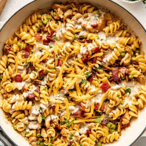 Overhead view of a skillet filled with One-Pot Chicken Bacon Ranch Pasta topped with bacon crumbles and melted shredded cheddar cheese.