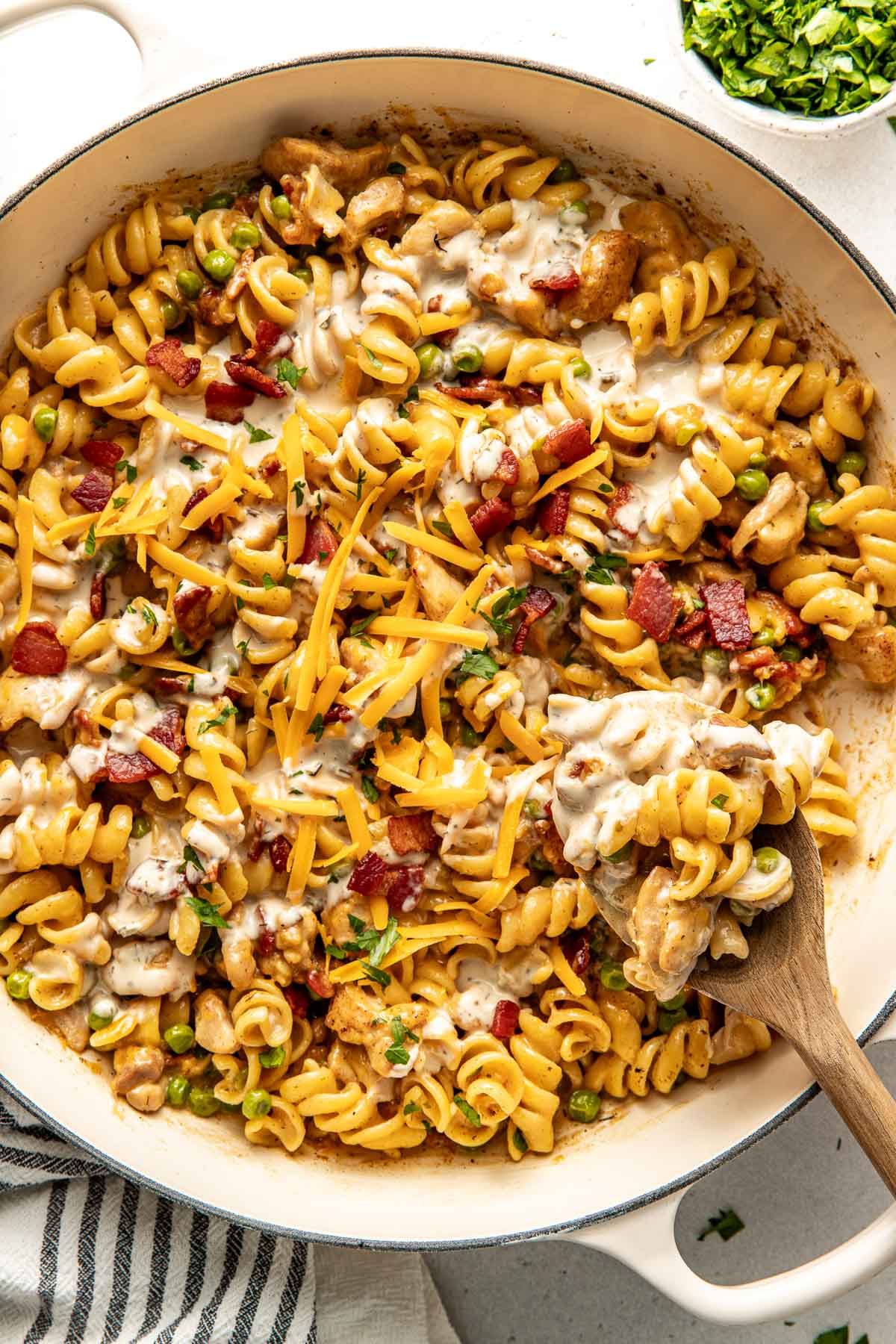 Overhead view of a skillet filled with One-Pot Chicken Bacon Ranch Pasta topped with crisp bacon pieces and shredded cheddar cheese. 