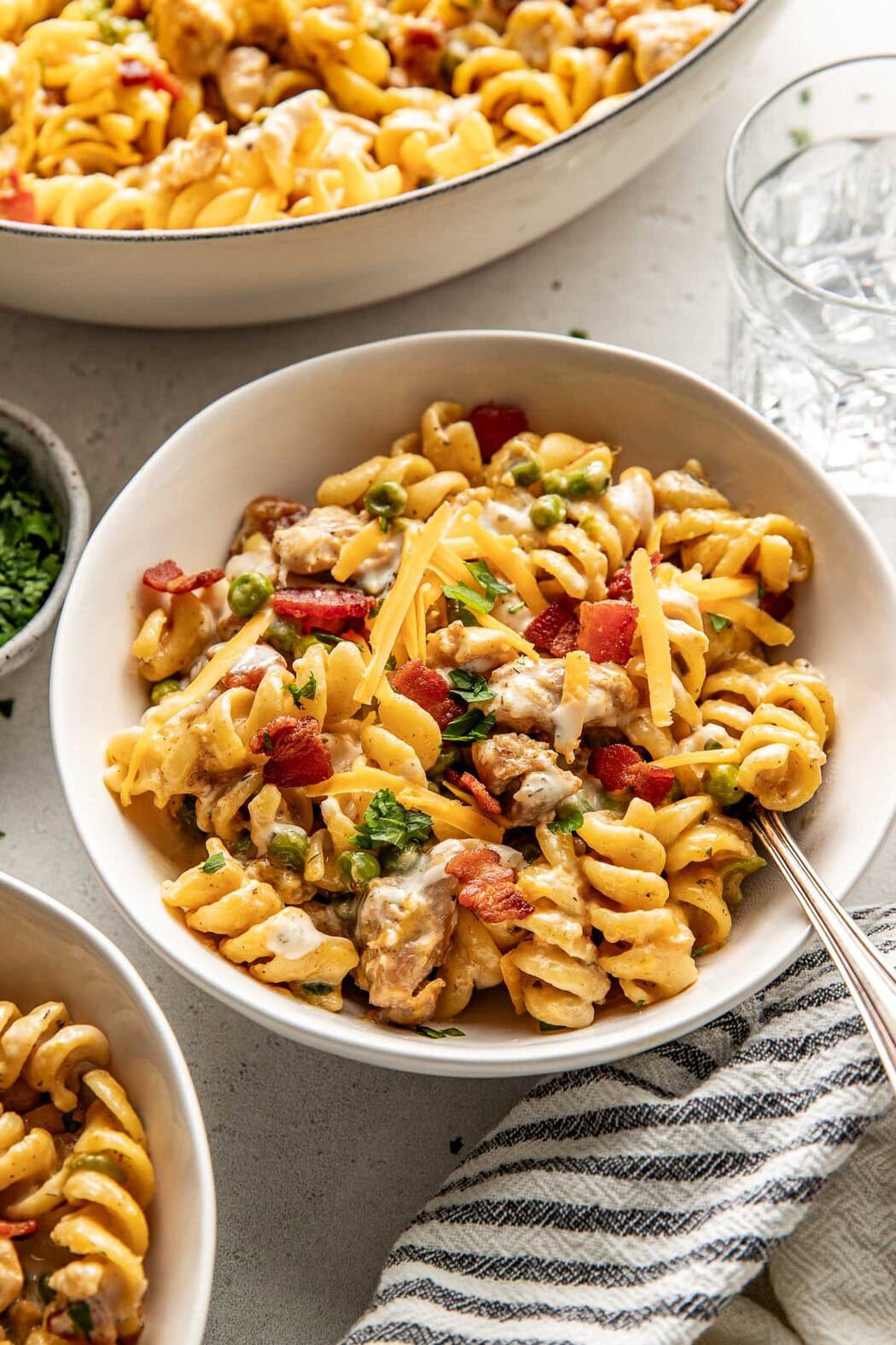 Close up view of a white bowl filled with One-Pot Chicken Bacon Ranch Pasta topped with melty shredded cheddar cheese. 