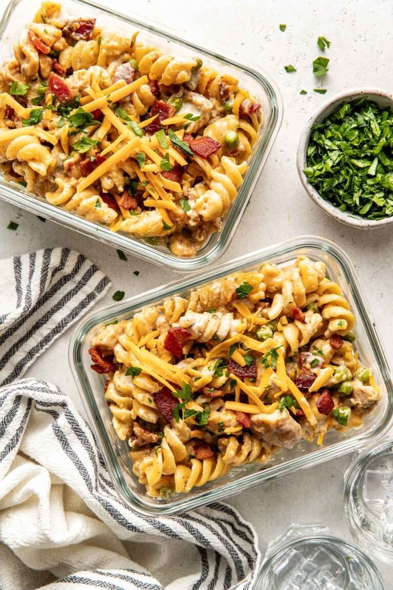 Overhead view of two glass meal prep containers filled with chicken bacon ranch pasta topped with melted cheese and sprinkled with fresh herbs.