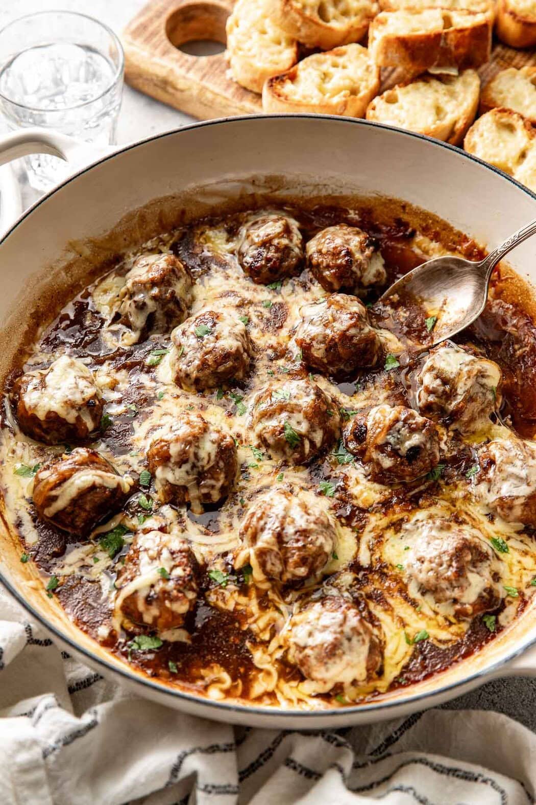Close up view of a skillet filled with French Onion Meatballs topped with melted cheese. 
