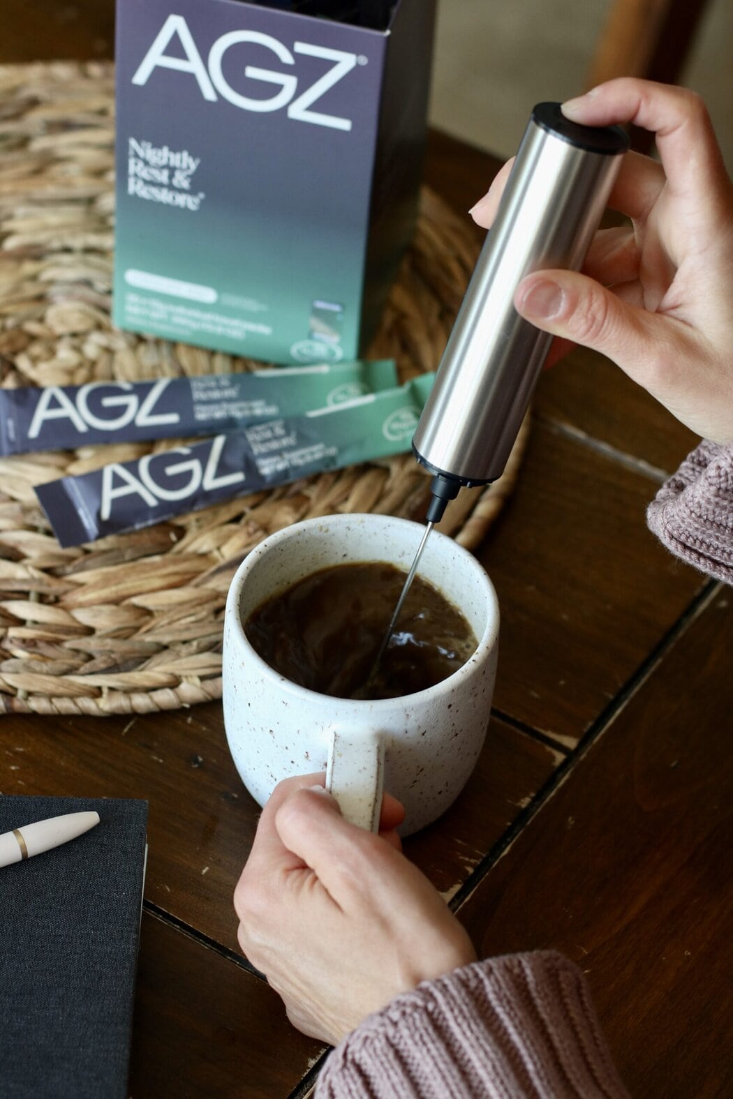 Close up view of a womans hand using a frother to mix a cup of AGZ nighttime drink. 