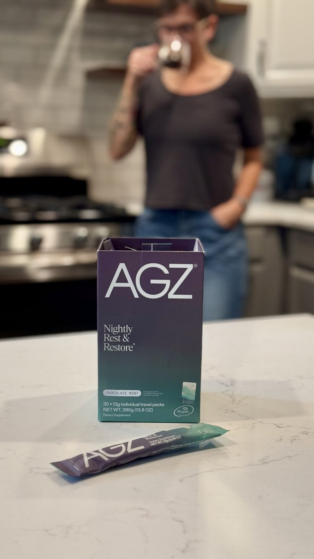 Close up view of a box and packet of AGZ nightly restore drink mix with a woman standing in the background. 