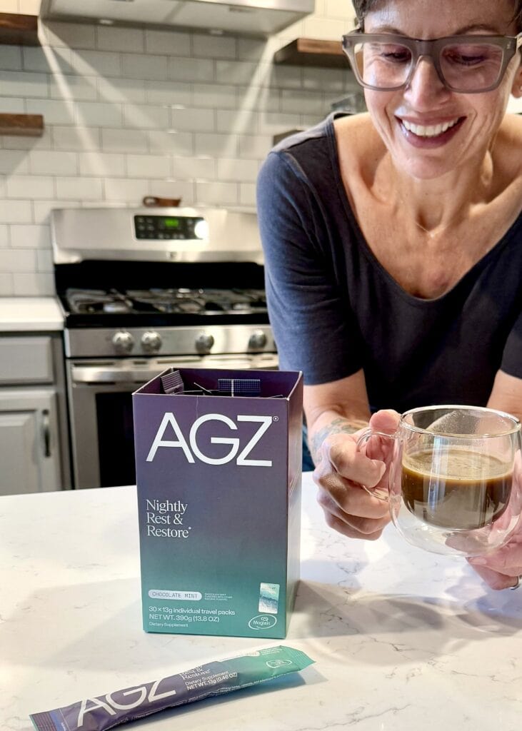 A woman at a countertop in a kitchen looking down at her AGZ nighttime drink in a glass mug. 