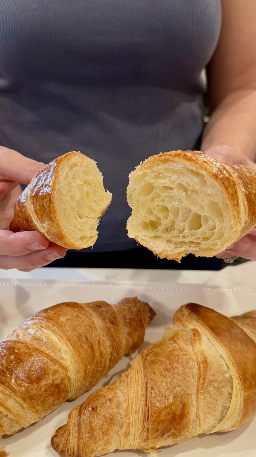 Close up view of a woman holding a freshly baked croissant cut in half to show the fluffy light texture of the inside. 