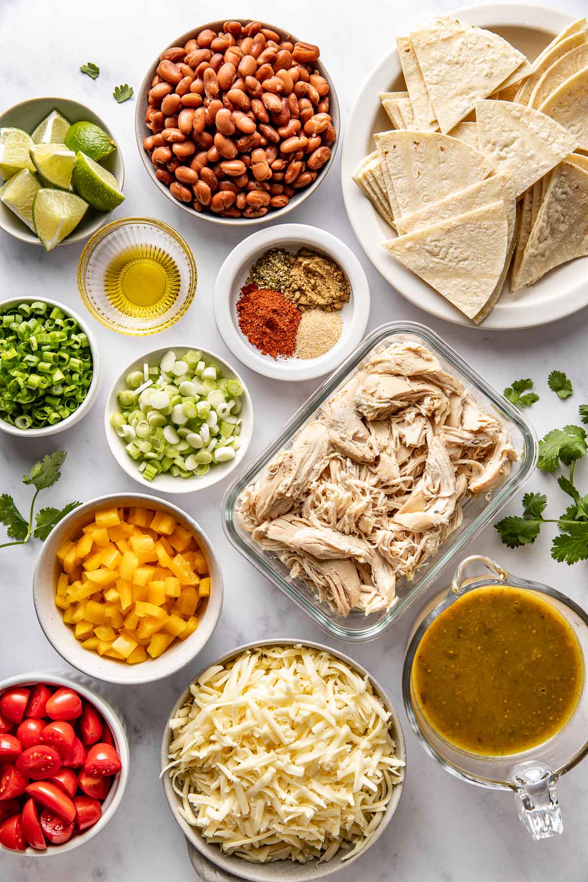 Overhead view of a variety of ingredients for Skillet Chicken Enchiladas in different sized bowls. 