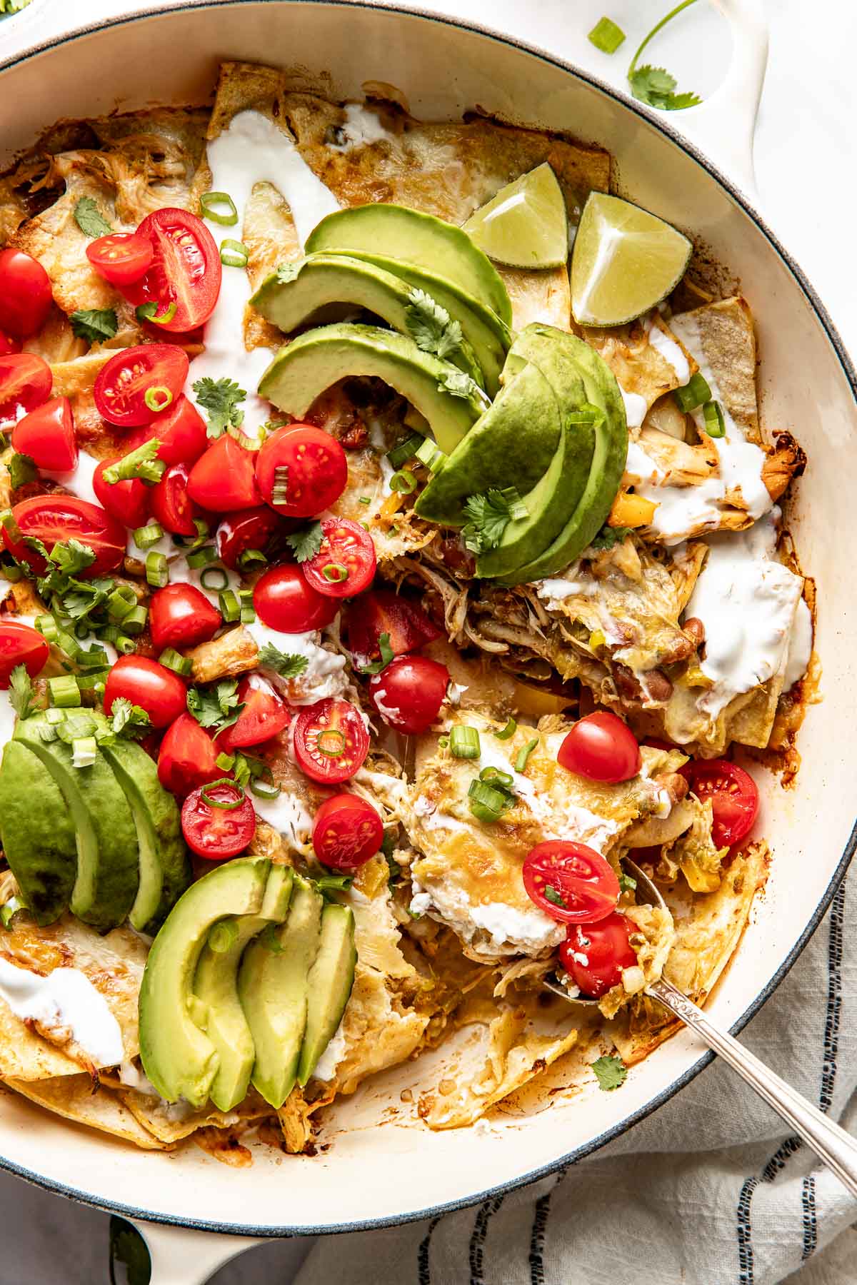 Close up view of a skillet filled with chicken enchiladas and topped with avocado and tomatoes. 