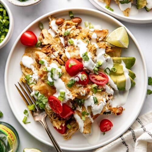 Overhead view of a white plate filled with chicken enchiladas skillet topped with sour cream and sliced tomatoes.