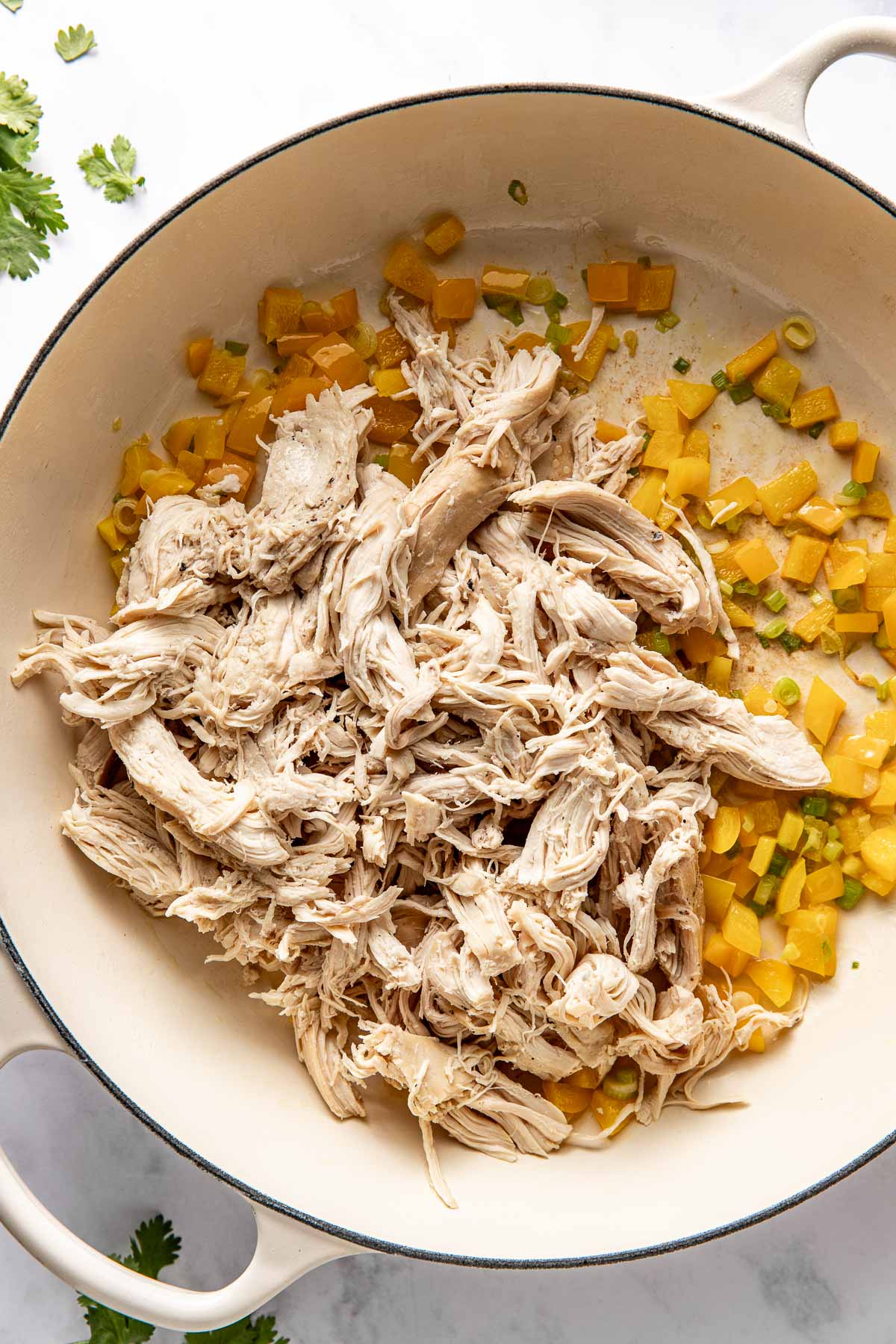 Overhead view of a skillet with peppers and onions sautéing with shredded chicken breast on top.  