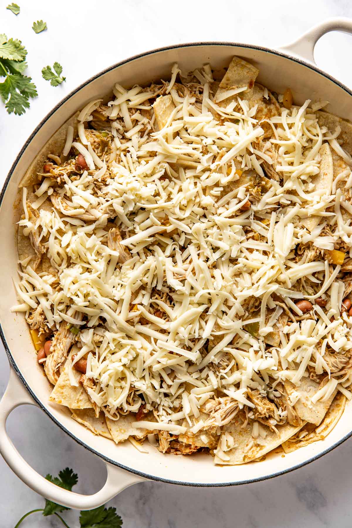 Overhead view of a skillet filled with chicken enchiladas ingredients and topped with shredded cheese. 