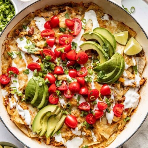 Overhead view of a skillet filled with Chicken Enchiladas topped with avocado and tomatoes.