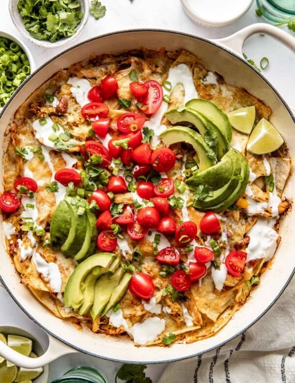 Overhead view of a skillet filled with Chicken Enchiladas topped with avocado and tomatoes.