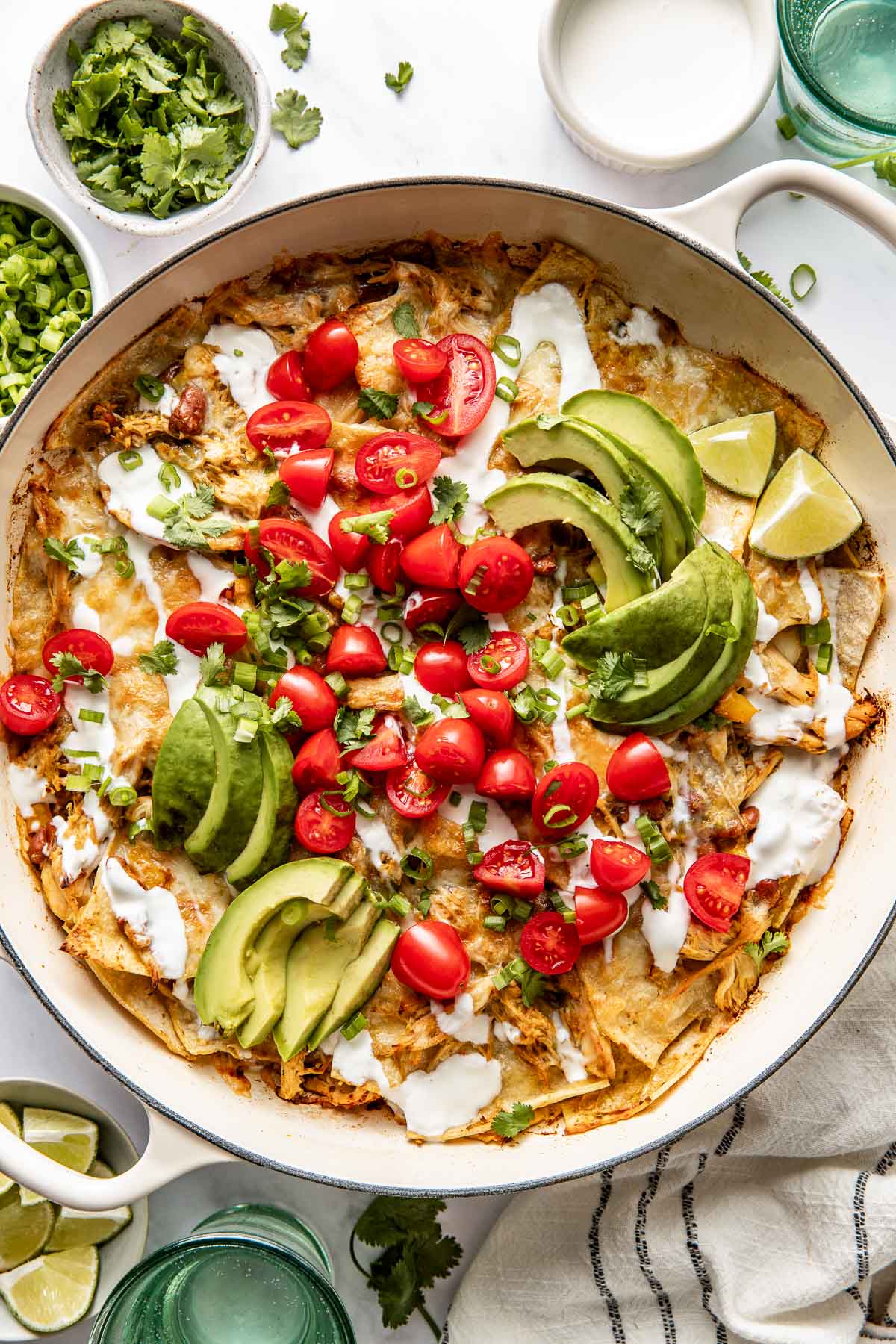 Overhead view of a skillet filled with chicken enchiladas topped with sour cream, avocado, and tomatoes. 