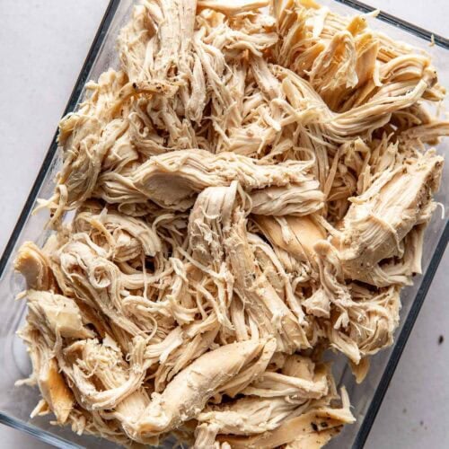 A clear glass container filled with leftover shredded chicken.
