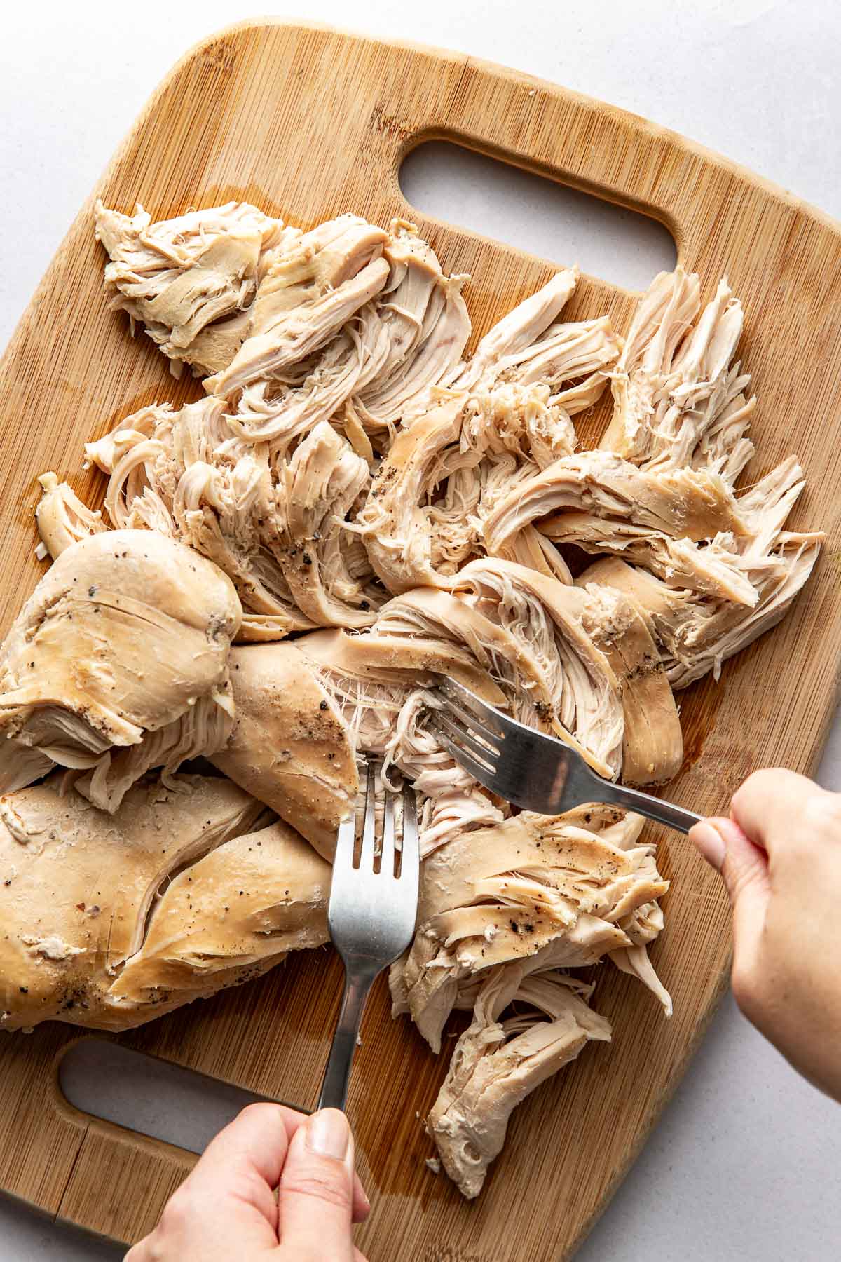 Overhead view of a wooden cutting board filled with shredded chicken breasts.