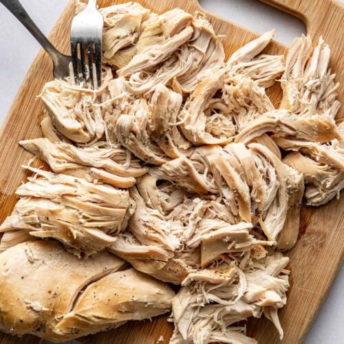 A cutting board piled with shredded chicken breast.