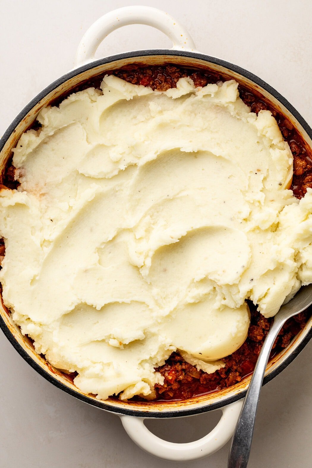 Overhead view of a skillet of sloppy joe meat with mashed potatoes spread over the top.