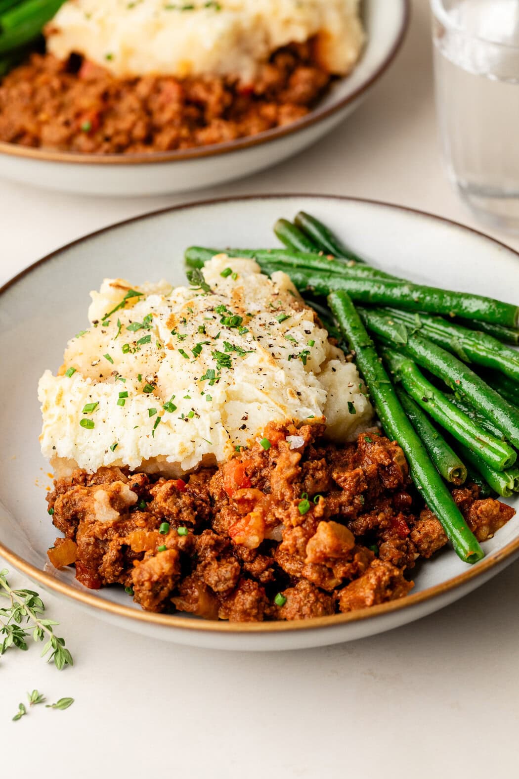 Close up view of a plate of Sloppy Joe Casserole with green beans on the side topped with fresh herbs and black pepper. 