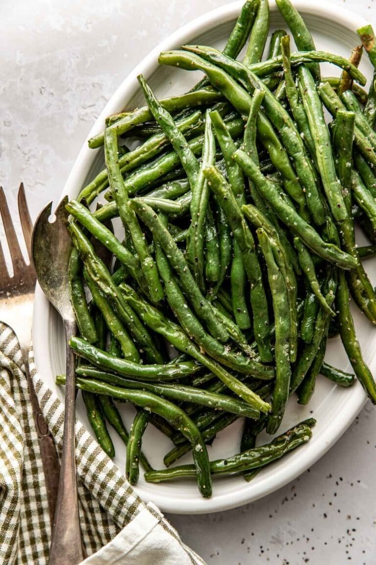 Overhead view of a platter filled with freshly roasted green beans topped with sat and pepper and garnished with lemon.