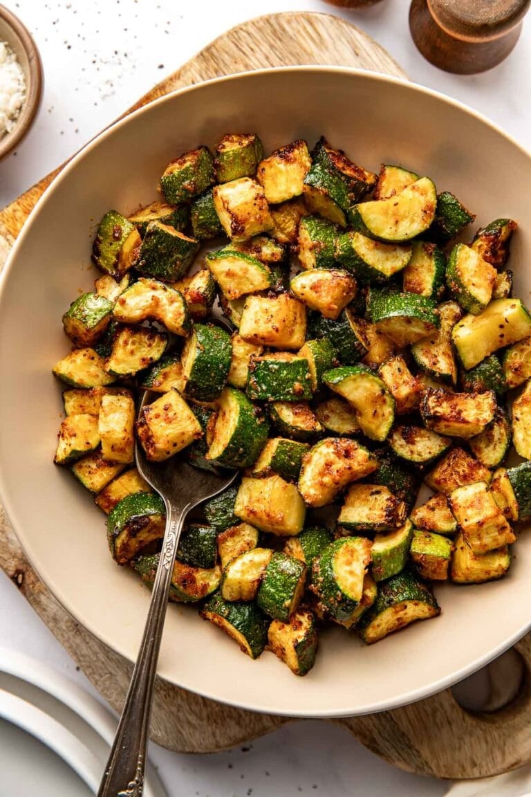 Overhead view of a ceramic bowl filled with crisp Air Fryer Zucchini pieces with a spoon in the bowl.