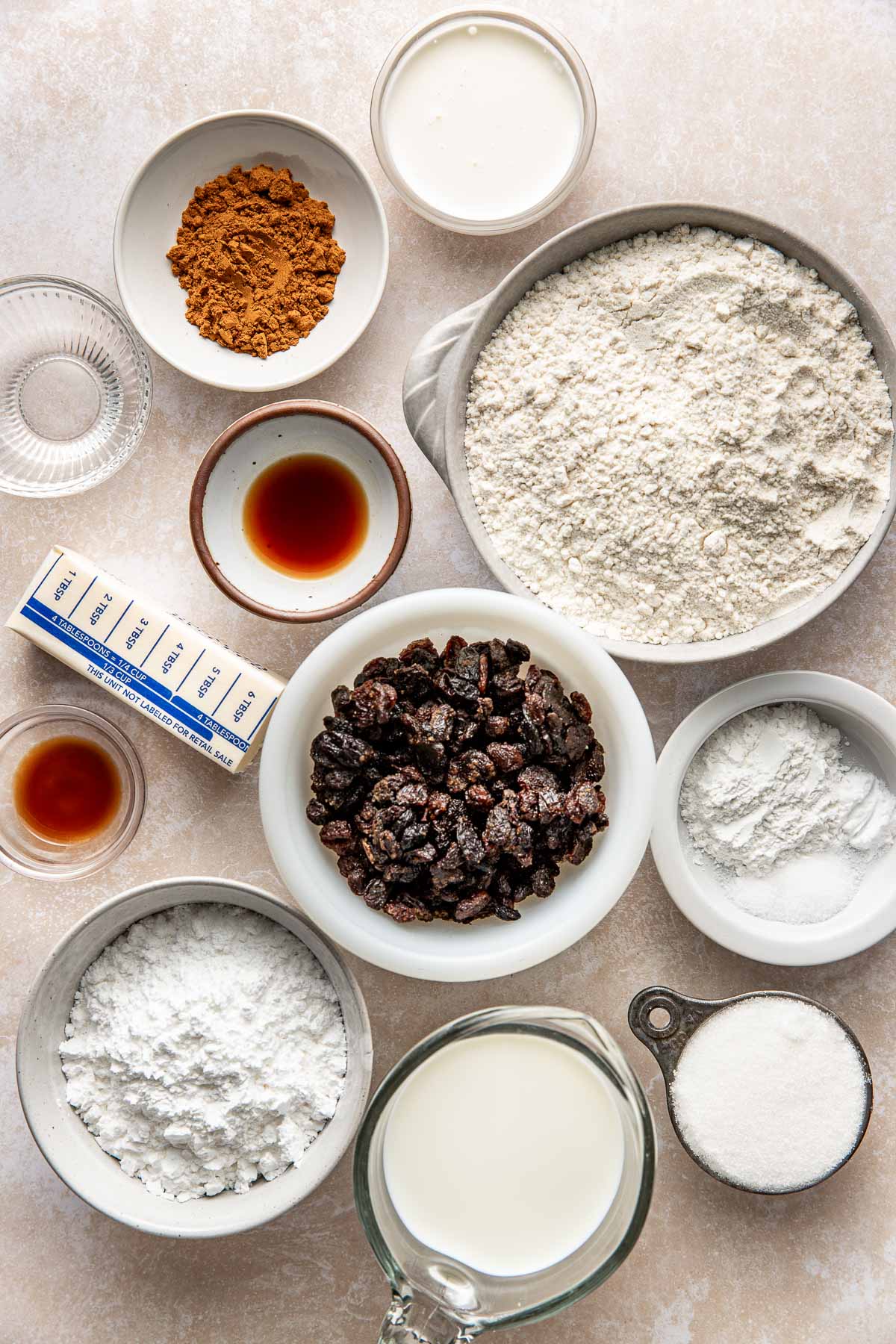 A stick of butter and multiple bowls filled with ingredients to make cinnamon raisin biscuits.