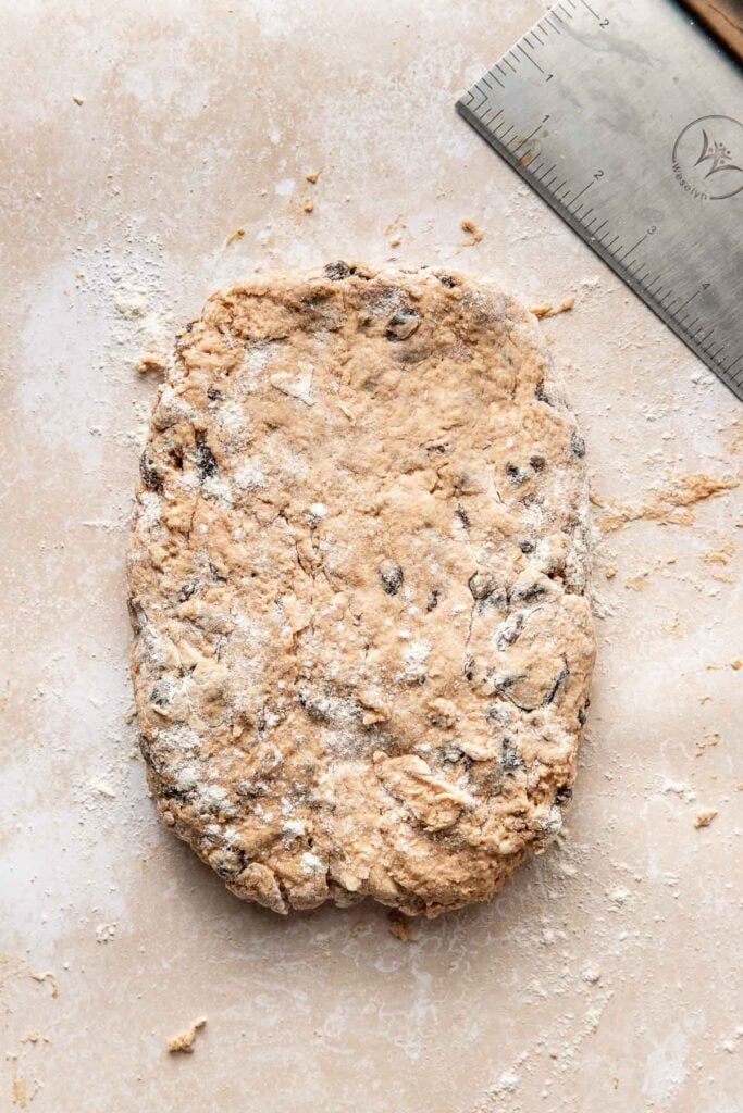 A flour dusted rectangle of cinnamon raisin biscuit dough and a bench scraper.