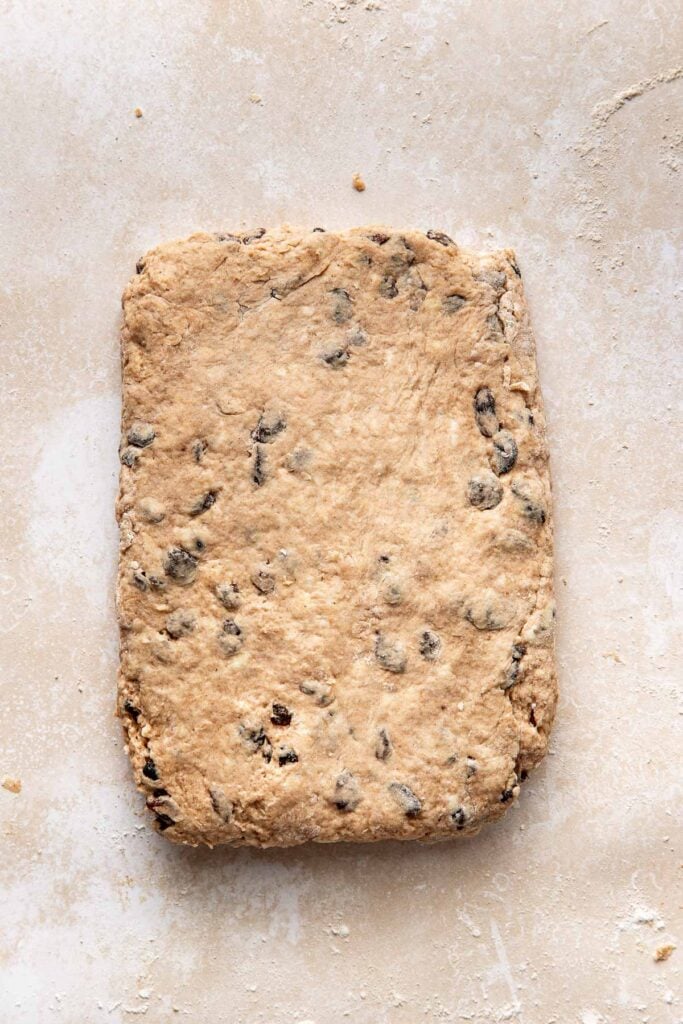 Light brown cinnamon raisin biscuit dough that has been patted into a large rectangle.
