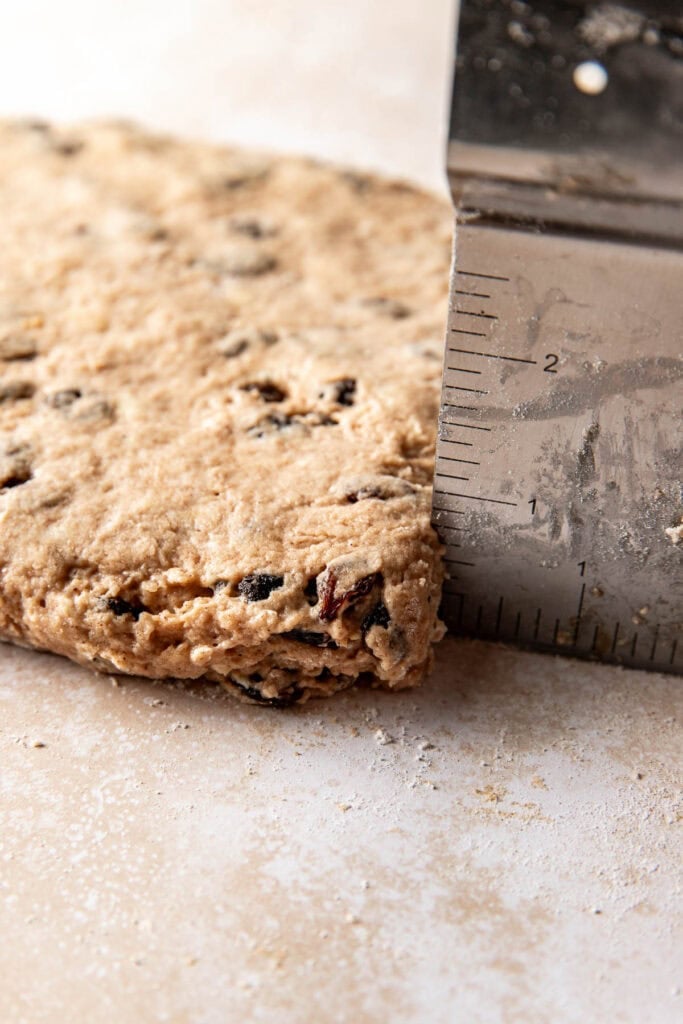 A bench scraper with measurements marked on its edge placed next to biscuit dough to show that it has been patted out to ¾ inch thickness.