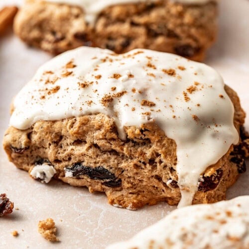 A close up view of cinnamon raisin biscuit topped with vanilla glaze and a sprinkle of cinnamon.
