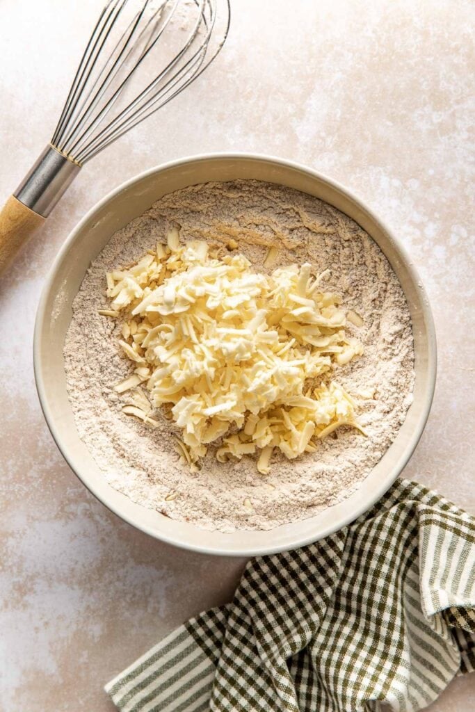A bowl of dry ingredients topped with mound of grated butter.