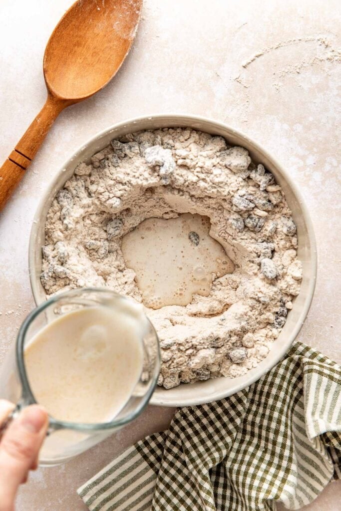 Pouring a milk, vanilla and vinegar mixture from a measuring cup into well in the bowl of flour.