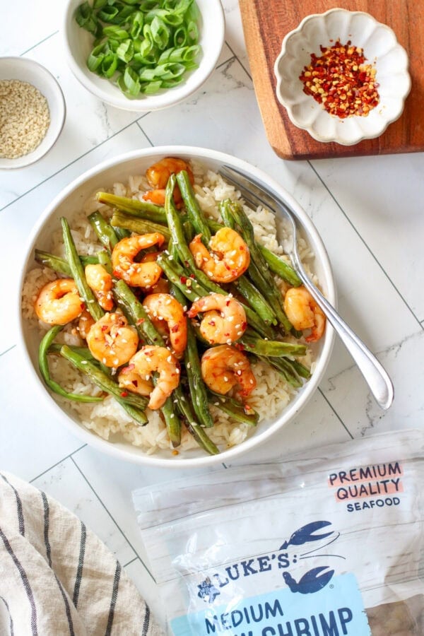 A shallow white bowl filled with rice and topped with honey garlic shrimp.