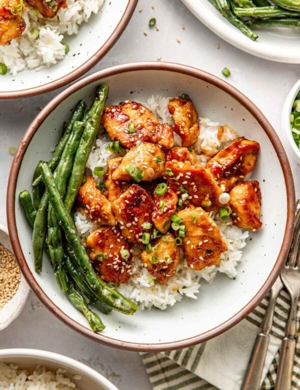 Overhead view of a plate filled with white rice, sesame chicken pieces, and roasted green beans.