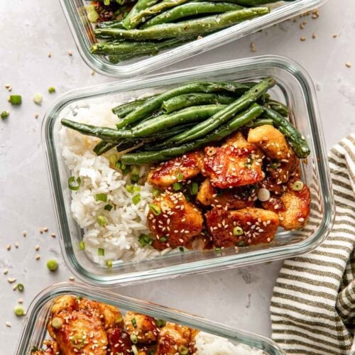 Overhead view of a glass meal prep container filled with green beans, rice, and sesame chicken.