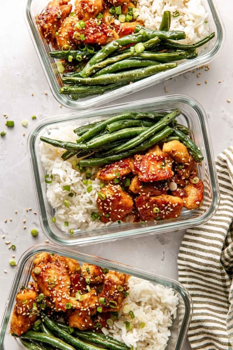 Overhead view of a glass meal prep container filled with green beans, rice, and sesame chicken.