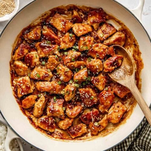 Overhead view of a skillet filled with sesame chicken in sauce and topped with sesame seeds.