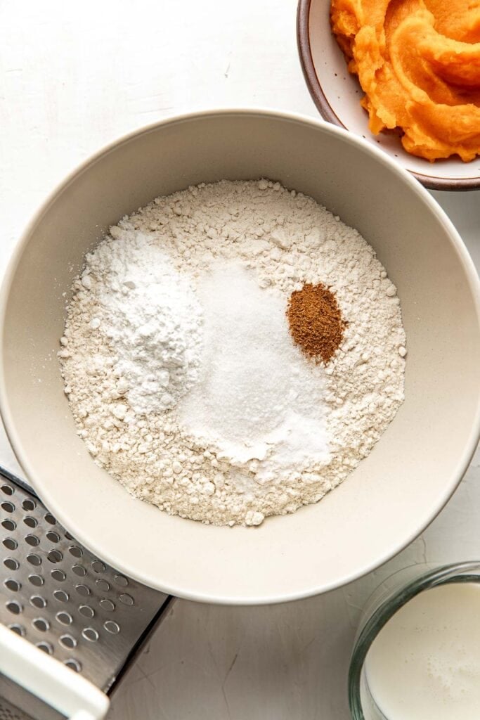 A bowl filled with flour, sugar, leavening agents and nutmeg to make sweet potato biscuits from scratch.