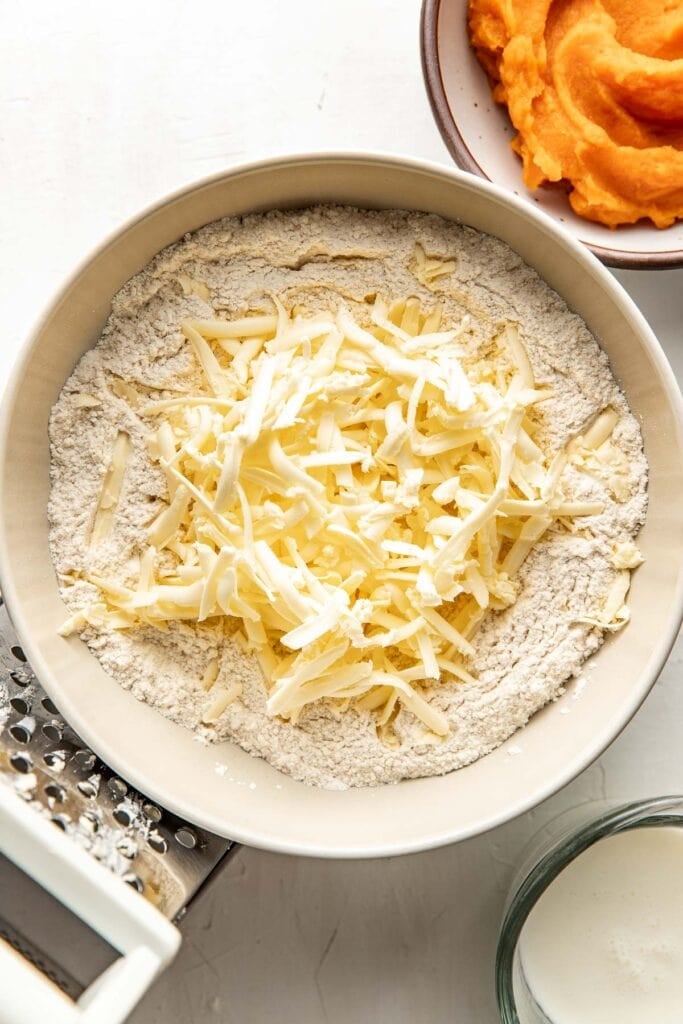 A white bowl filled with flour and topped with butter that has been grated on a box grater.