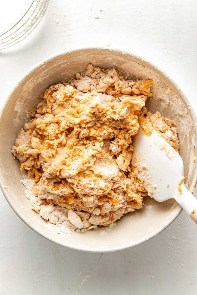A bowl of sweet potato biscuit dough that has been partially mixed together using a spatula.