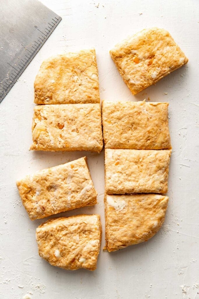8 squares of unbaked sweet potato biscuit dough arranged on a white counter next to a bench scraper.