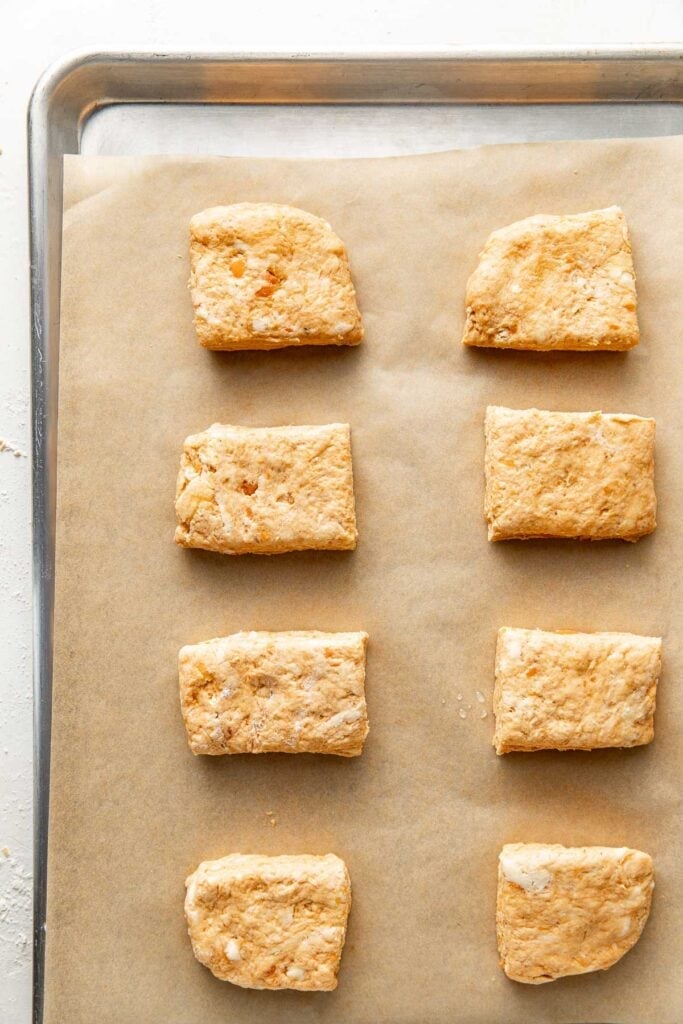 8 unbaked sweet potato biscuits arranged on a silver baking sheet lined with parchment paper.