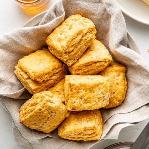 A bowl lined with a light colored linen napkin and filled with jewel-toned sweet potato biscuits.