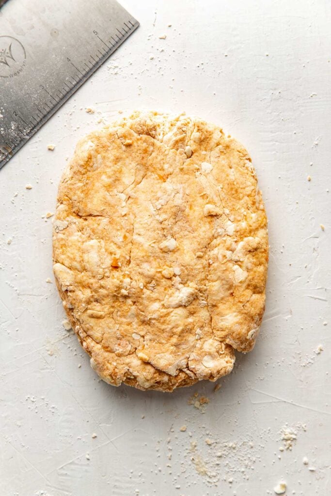 An overhead view of sweet potato biscuit dough that has been patted into a rectangle on a white countertop.
