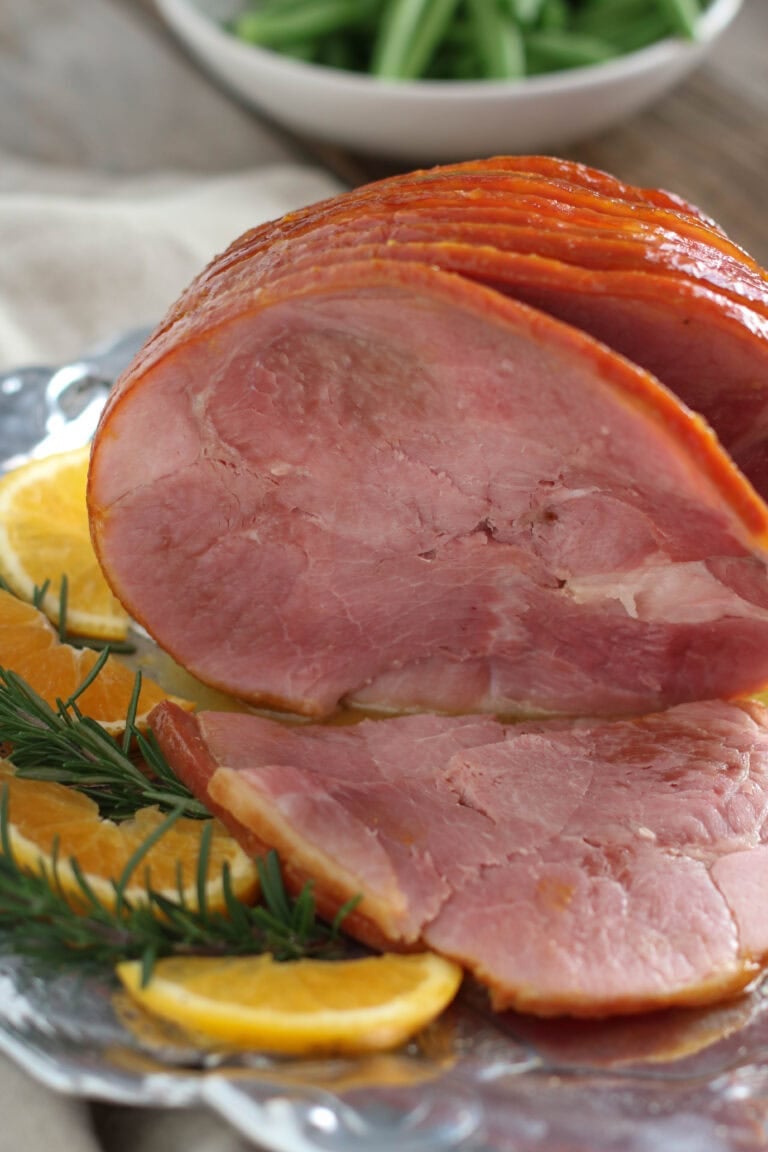 Close up view of a sliced baked ham with orange slices on the side. 