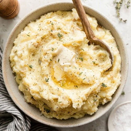 Overhead view of a bowl of freshly mash potatoes topped with fresh herbs and melted butter.